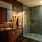 Clérachic gold wall light with a crystal centrepiece beside a mirror on a wood-panelled bathroom wall, next to a glass shower.