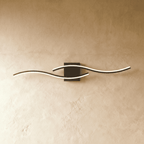 Clérachic black wavy bar wall lamp lit warm, two slim diffuser strips crossing over a square dark backplate.