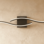 Close view of the Clérachic black wall lamp, showing the lit diffuser strips curving past a square matte backplate.