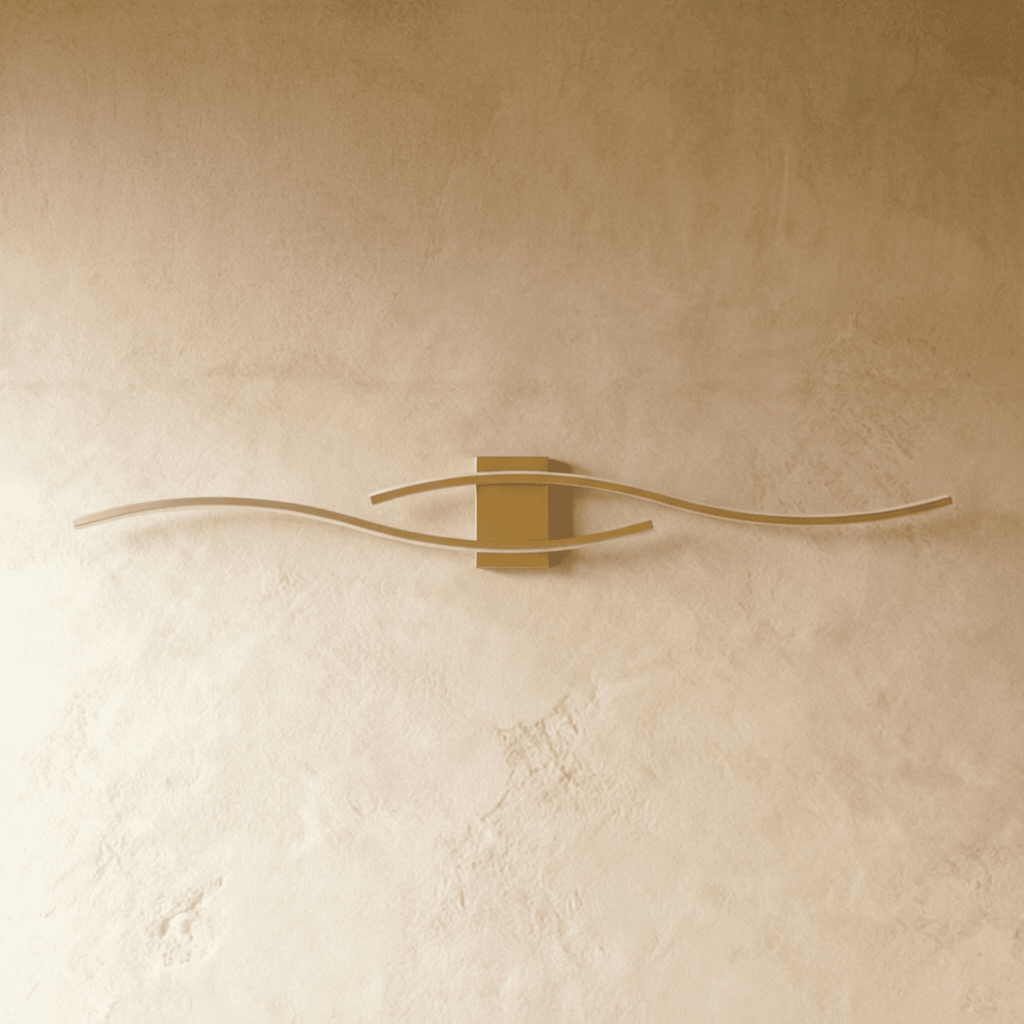 Clérachic gold wall lamp with two long wavy bars and a small rectangular backplate, shown unlit on a warm wall.