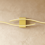 Close view of the Clérachic gold wall lamp's rectangular backplate and two softly glowing wavy diffuser bars.