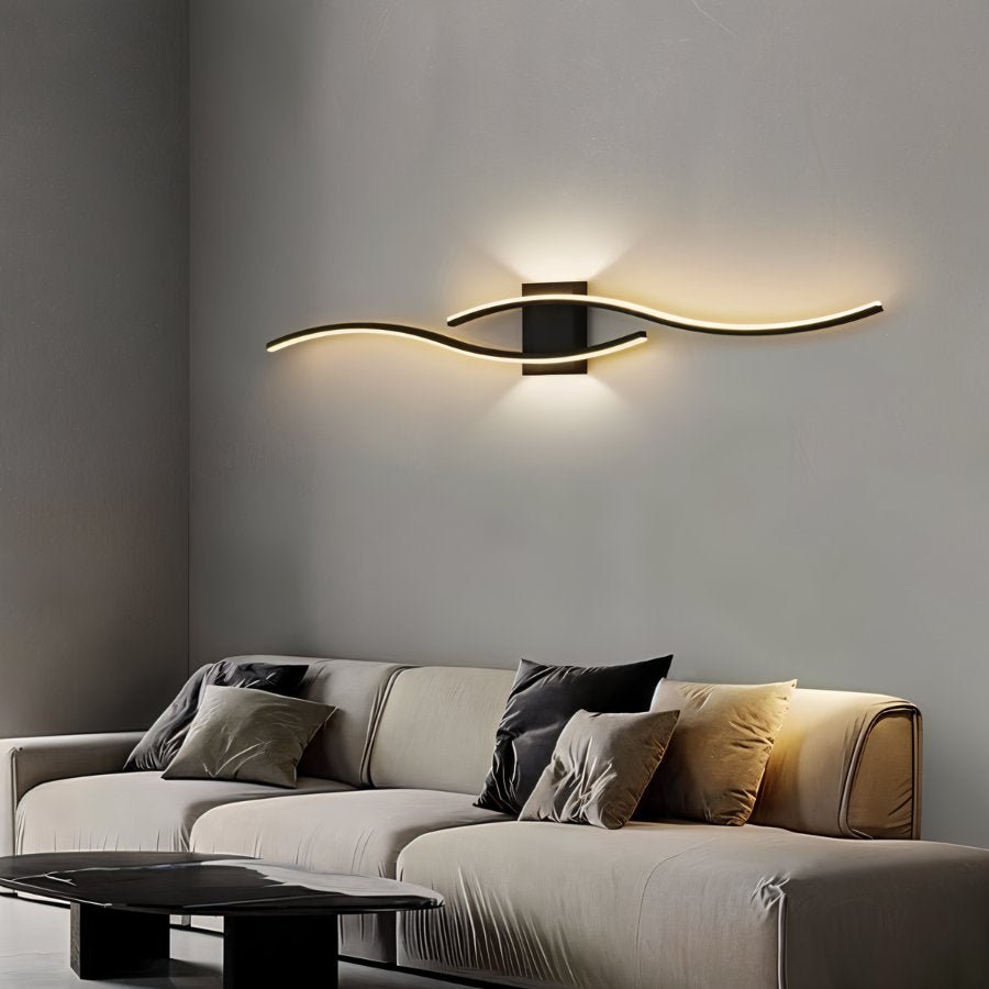Clérachic black wavy LED wall lamp glowing warm above a pale sofa with grey and black cushions in a living room.