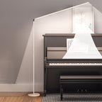 White Clérachic floor lamp with its light bar along the wall beside an upright piano, with a drawn beam of light falling onto the sheet music.