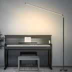 Black Clérachic slim floor lamp with a light bar swung over a dark upright piano, casting a warm glow on the wall behind.