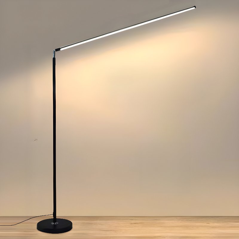 Black Clérachic floor lamp with a round base and a slim pole, its light bar lit and washing a warm glow over a beige wall.