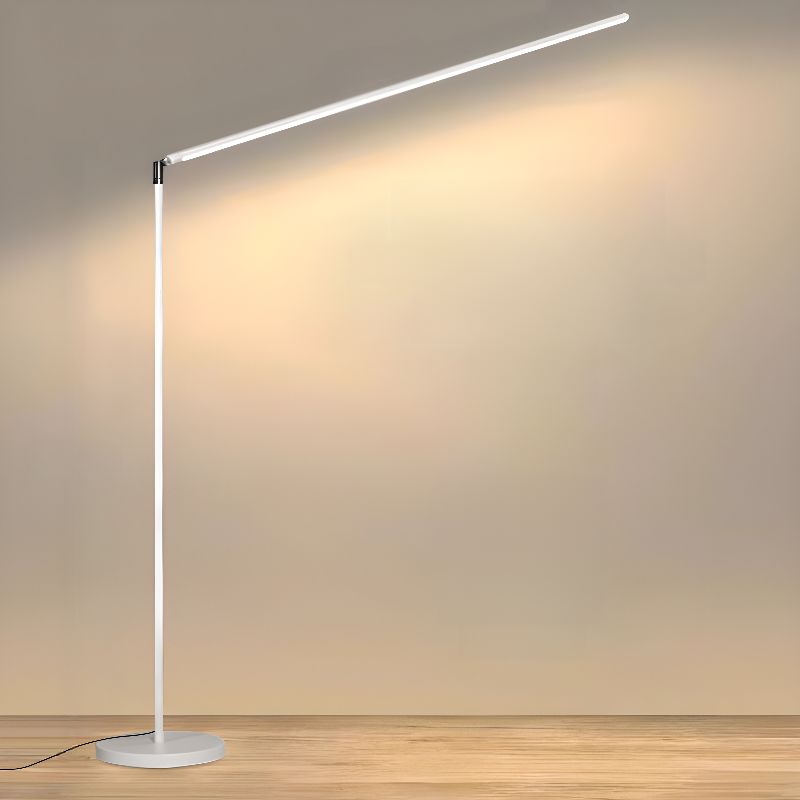 Clérachic floor lamp in white, its long light bar angled up to wash the wall with soft warm light, over a pale wood floor.