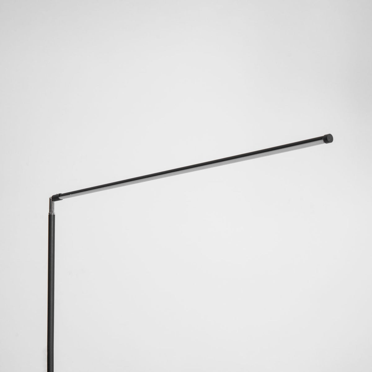 Close view of the pivot where the pole meets the long black light bar on this Clérachic floor lamp, unlit, on a pale grey backdrop.