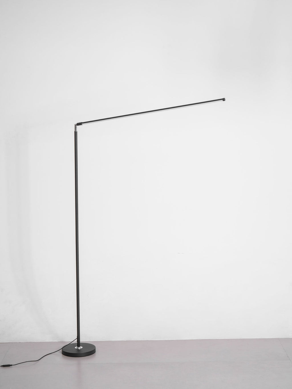 Unlit version of this Clérachic floor lamp with a black pole, a round base and a thin light bar held out at an angle, on grey.