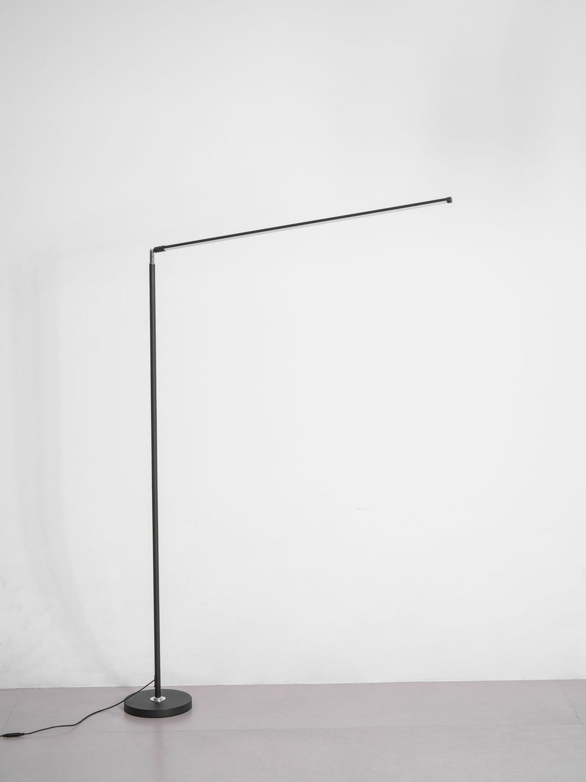 Unlit version of this Clérachic floor lamp with a black pole, a round base and a thin light bar held out at an angle, on grey.
