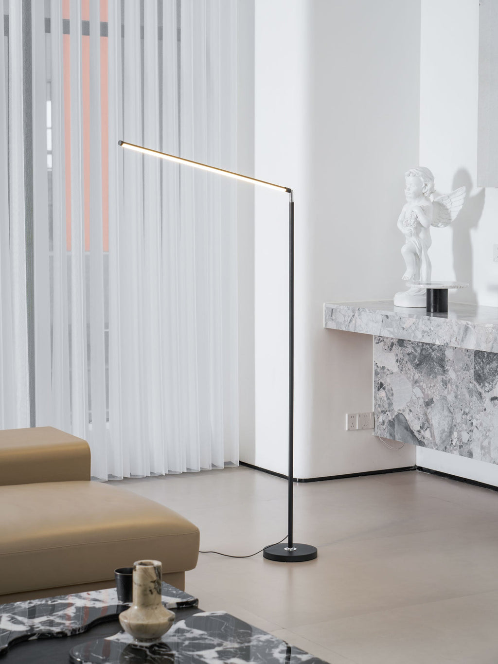 This Clérachic floor lamp stands beside a marble console, with its light bar lit, in front of sheer curtains and a tan sofa.