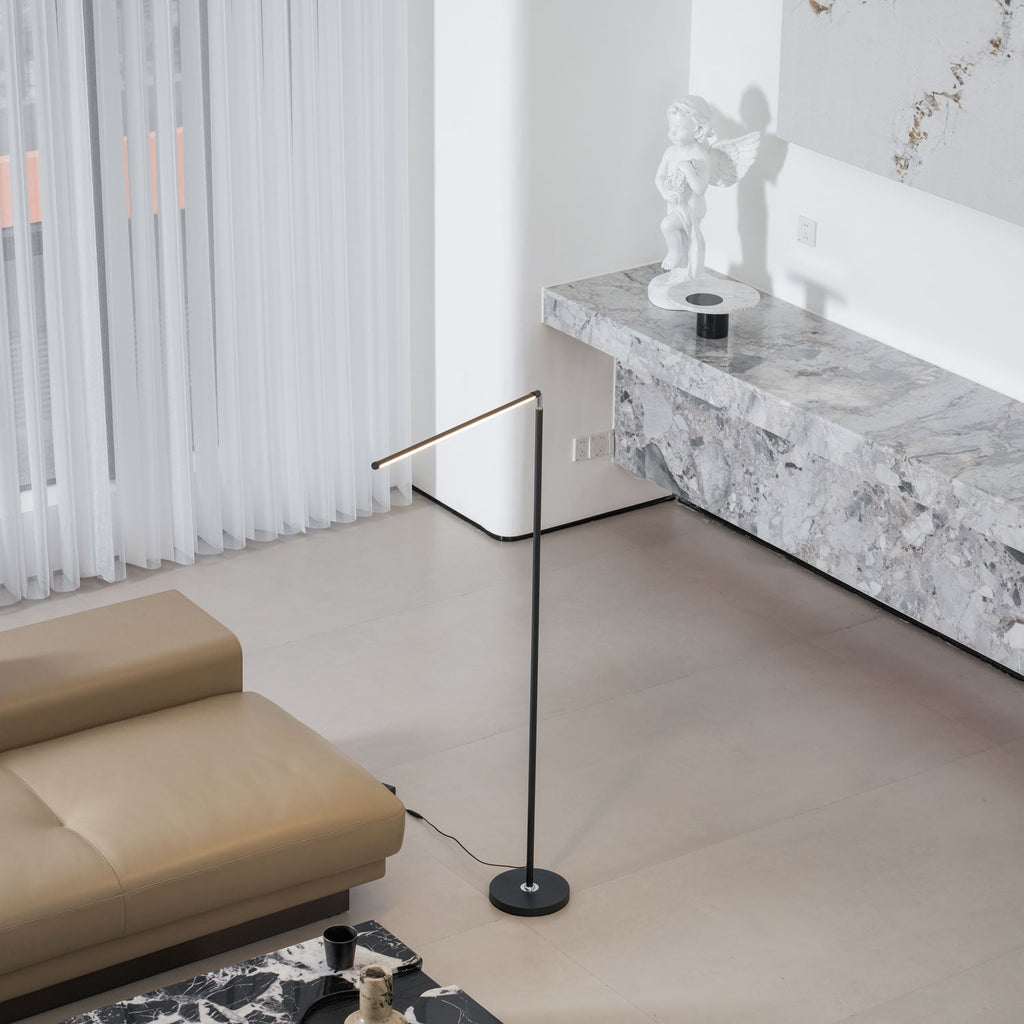 With its light bar angled down low, this Clérachic floor lamp stands between a tan leather sofa and a stone console in a bright room.