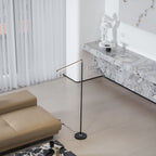 With its light bar angled down low, this Clérachic floor lamp stands between a tan leather sofa and a stone console in a bright room.