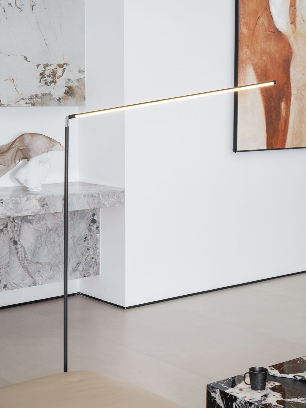 The lit light bar of this Clérachic floor lamp stretches out in front of a white wall, a stone console and a framed orange artwork.