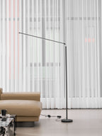 Black Clérachic floor lamp with the bar held out to the left, in front of sheer curtains and a tan sofa, with its cord on the floor.