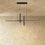 Clérachic slim black linear pendant with two suspended spotlight tubes, hung on thin wires against a limewash wall.