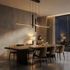 Clérachic black linear pendant glowing warmly over a timber dining table in a concrete-walled room at dusk.