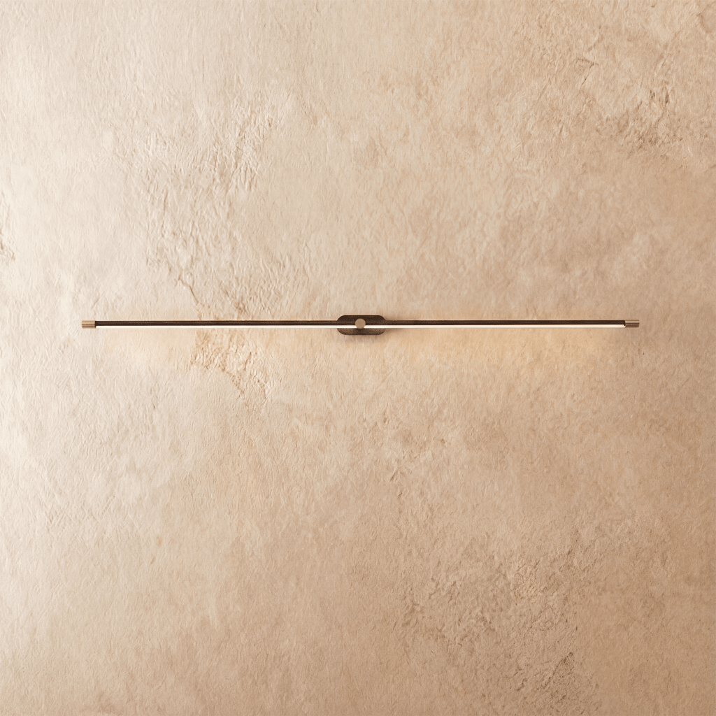 Clérachic ultra-slim linear wall light in black with gold end caps, glowing a thin warm line on a limewashed wall.