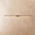 Clérachic ultra-slim linear wall light in black with gold end caps, glowing a thin warm line on a limewashed wall.
