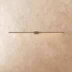 Clérachic ultra-slim linear wall light in black with gold end caps, glowing a thin warm line on a limewashed wall.