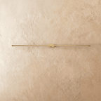 Clérachic ultra-slim linear wall light switched off, a gold aluminium bar with fluted end caps on a plaster wall.