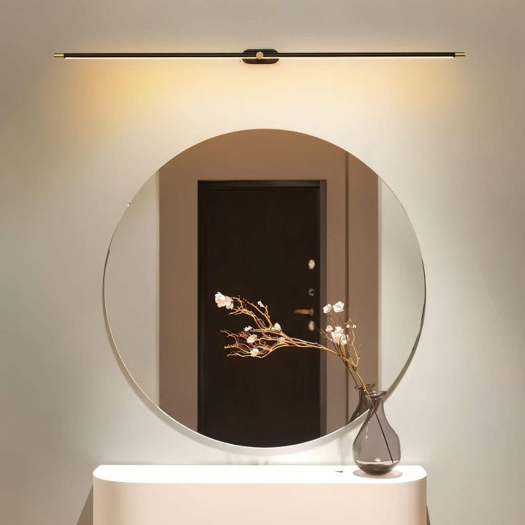 Clérachic slim black and gold bar light mounted above a large round mirror, washing the wall with soft warm light.