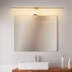 Clérachic slim gold bar light mounted above a rectangular vanity mirror, lit warm over a white basin and timber shelf.
