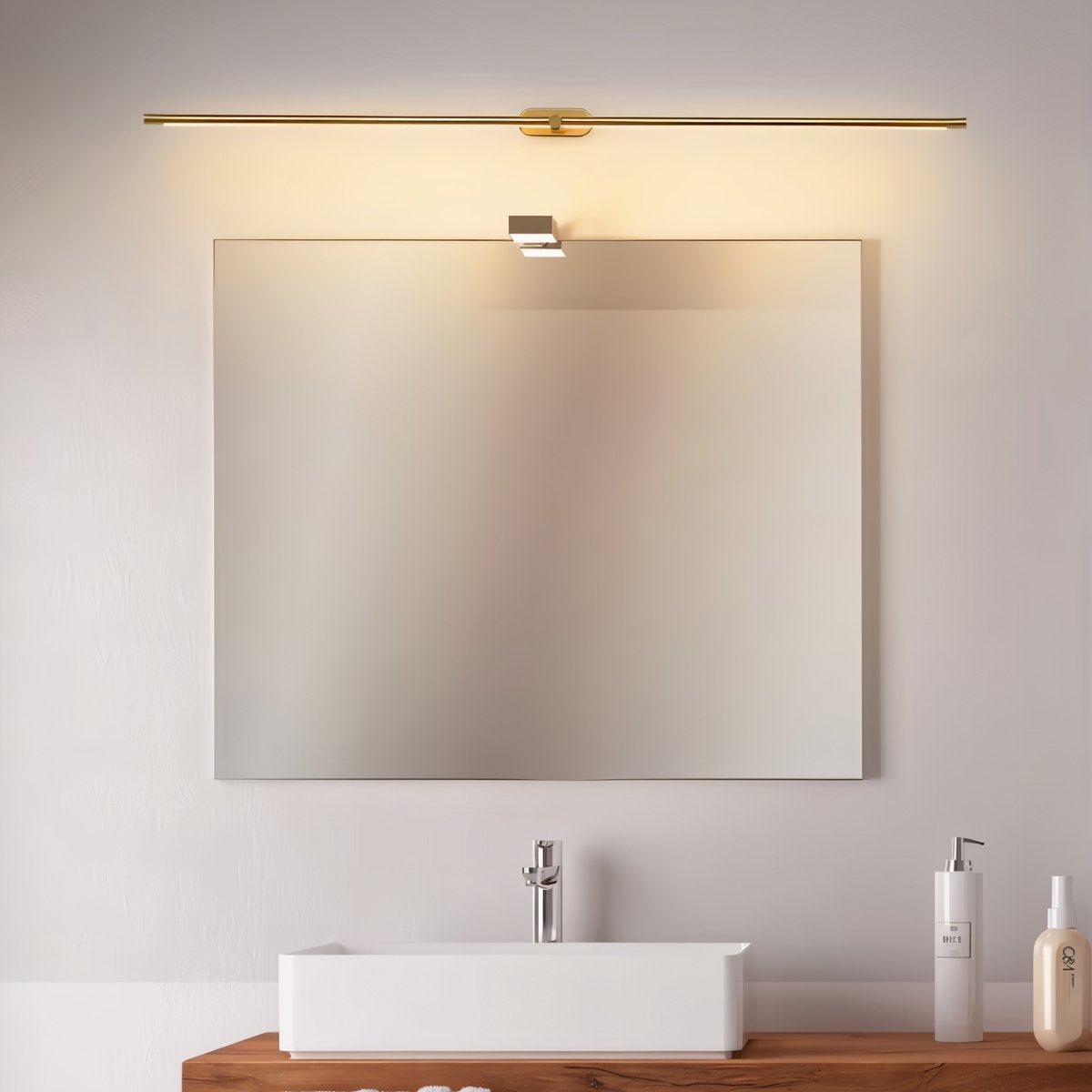 Clérachic slim gold bar light mounted above a rectangular vanity mirror, lit warm over a white basin and timber shelf.