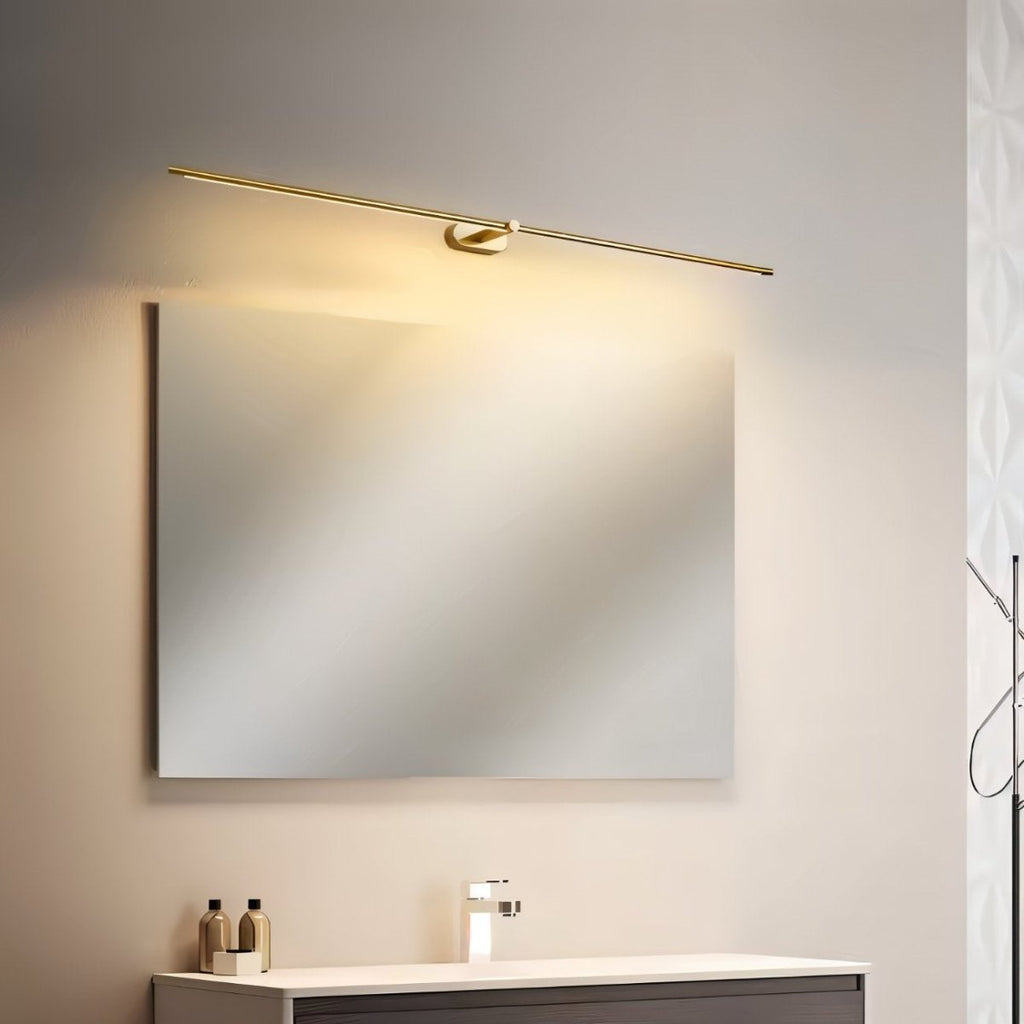Clérachic slim gold bar light set at a tilt above a wall mirror, casting warm light down over a vanity unit.