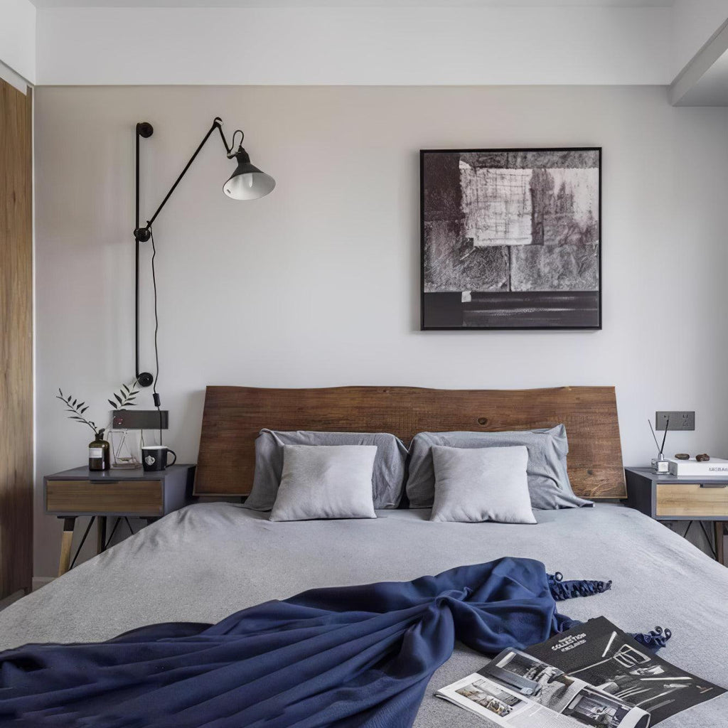 A Clérachic wall light with a pale cone shade above a bedside, on the wall beside a framed monochrome print and a wooden headboard.