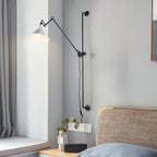 This Clérachic wall light has a white cone shade beside a window, with the cable dropping down the wall above a bed with a woven headboard.
