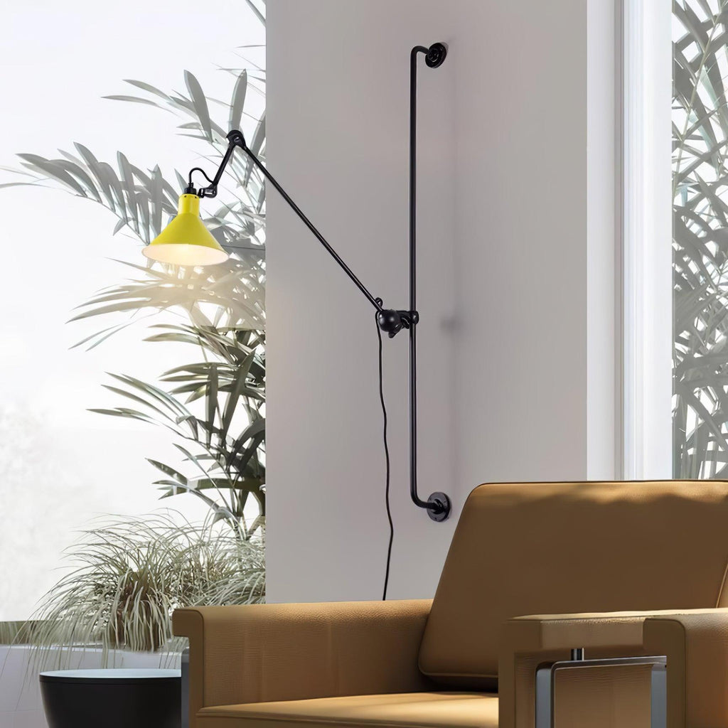 A Clérachic wall light with a yellow cone shade next to a tall window with palm leaves, above a tan leather armchair.