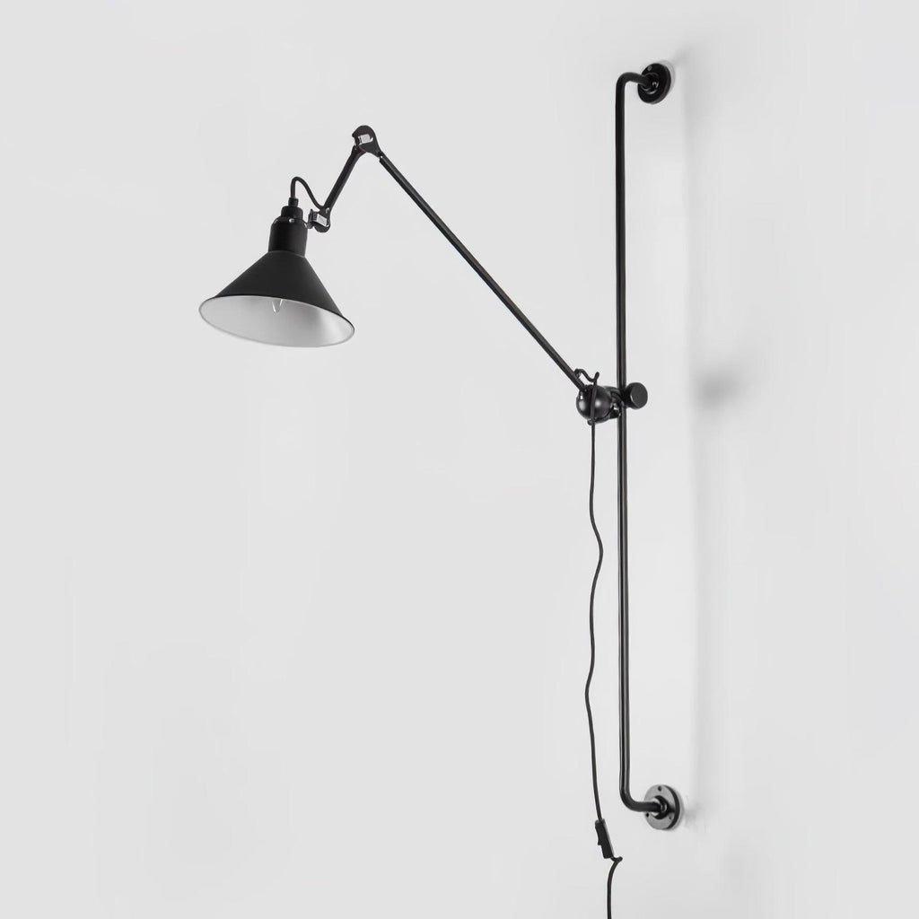 This Clérachic wall light on a plain white wall, with a long black bar, a hinged arm and a black cone shade with a white inner face.
