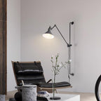 This Clérachic wall light has a white cone shade lit above a black leather lounge chair, with a stone side table and a flower stem.