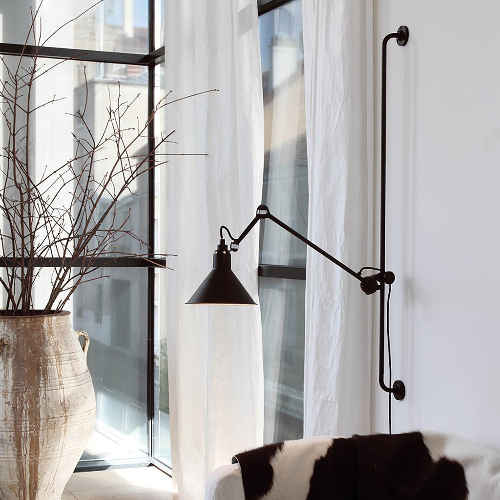 A Clérachic black wall light with a long arm and cone shade beside tall windows with white curtains and bare branches in a vase.