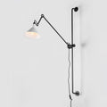 Shown here, a Clérachic wall light with a white cone shade on a long black bar, seen against a pale grey backdrop.