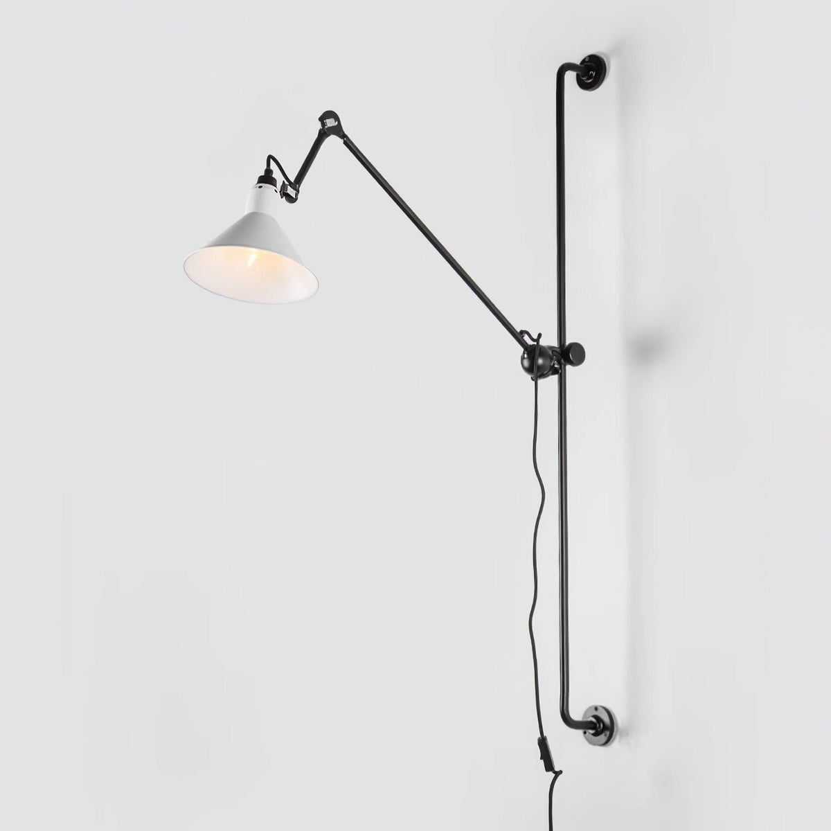 Shown here, a Clérachic wall light with a white cone shade on a long black bar, seen against a pale grey backdrop.