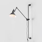 A Clérachic wall light with a grey cone shade on a long black bar, seen against a pale grey backdrop.