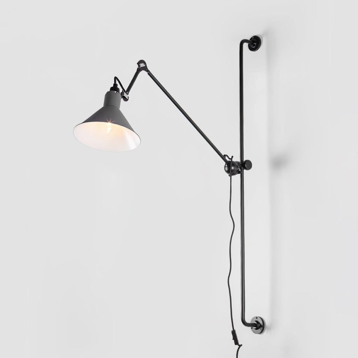 A Clérachic wall light with a grey cone shade on a long black bar, seen against a pale grey backdrop.