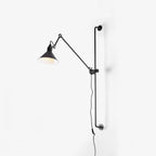 A Clérachic wall light with a dark cone shade on a slim black bar, shown against a plain white backdrop with its cable hanging below.