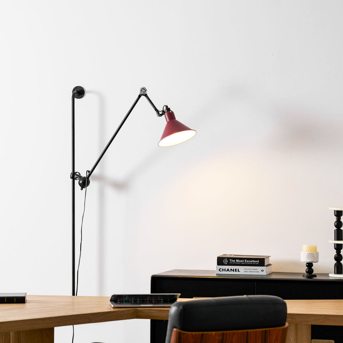 Shown here, a Clérachic wall light with a red shade above a desk with a stack of books, a tablet and a black sideboard, in a bright room.