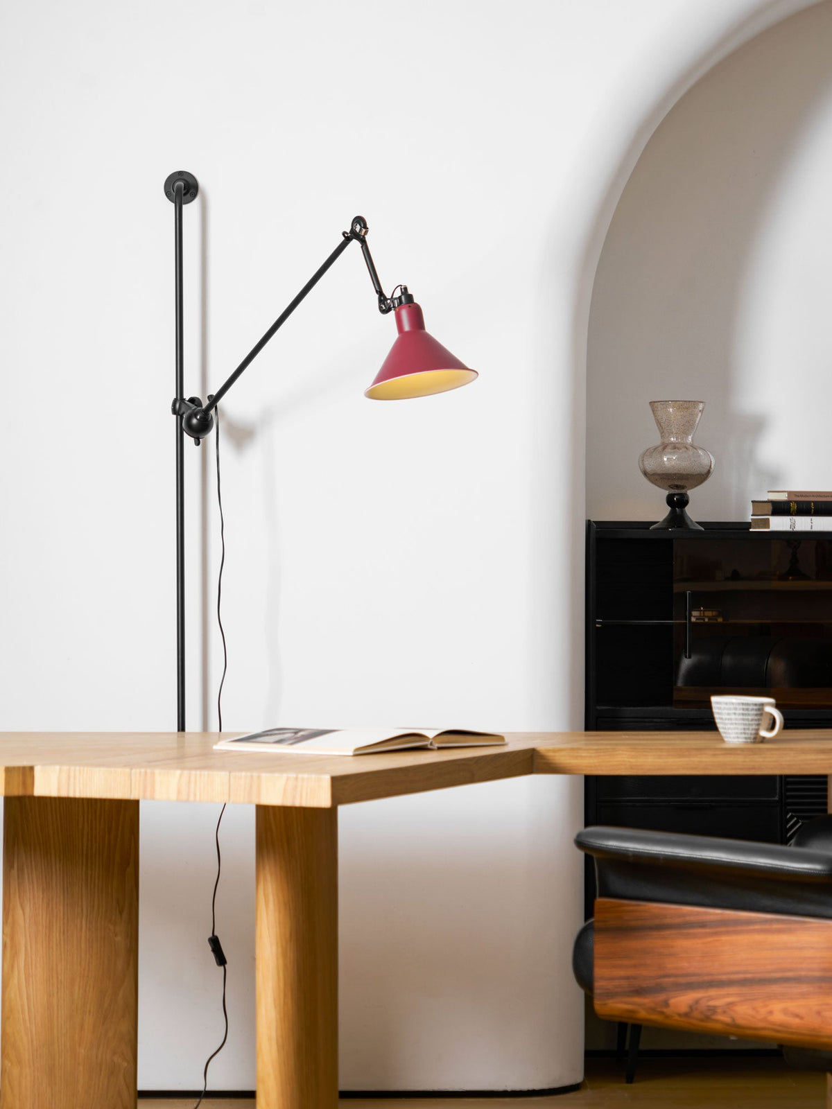 Close view of the red metal shade, small brass-coloured vent holes and black socket cap on this Clérachic wall light.