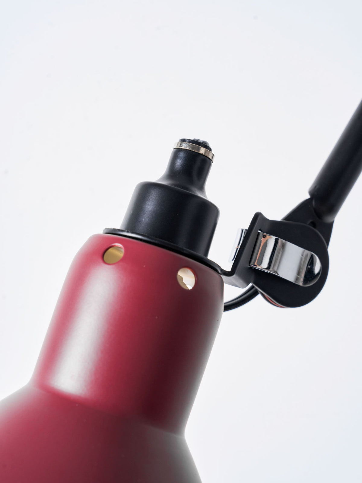 Close view of the matt red cone shade with its vent holes and the black lamp holder on this Clérachic wall light.