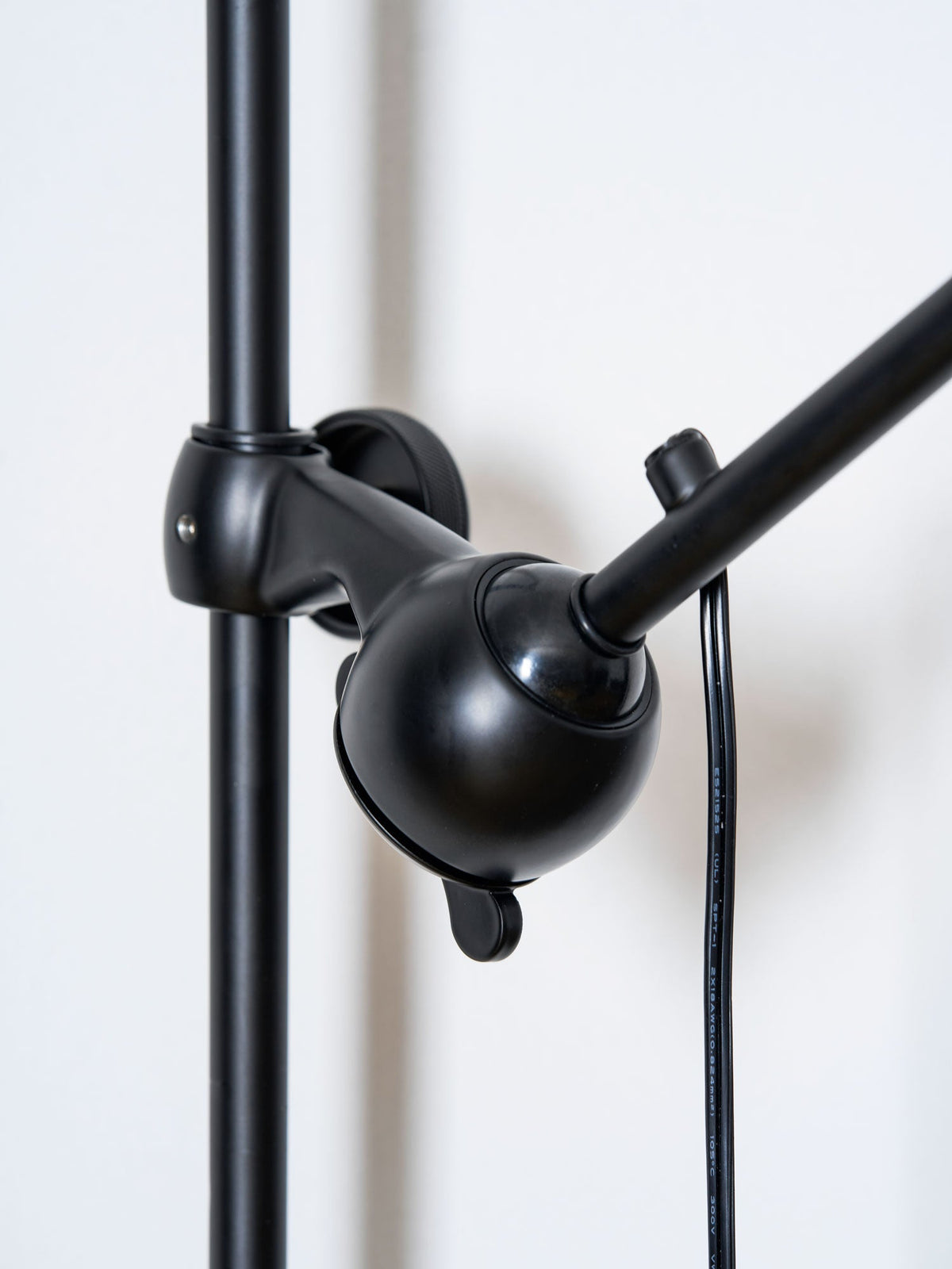 A Clérachic wall light with a red cone shade on a slim black bar, shown small against a white wall with the cable hanging below.