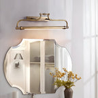 This Clérachic wall light glowing warm above a bevelled bathroom mirror, with a vase of yellow flowers beside it.