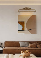 A Clérachic wall light above an abstract painting, with a brown leather sofa and a bowl of walnuts in the room below.