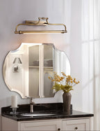 This Clérachic wall light mounted over a scalloped mirror and a dark marble vanity with a chrome tap.