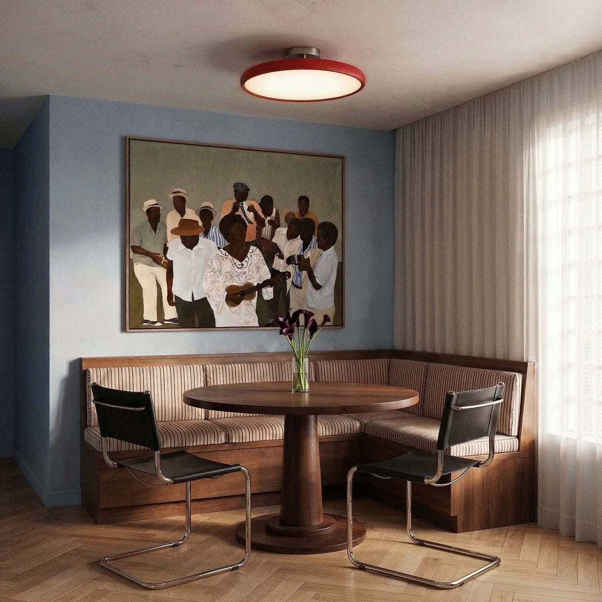 Clérachic red round ceiling light glowing over a corner dining nook with a walnut table, striped banquette and large painting.