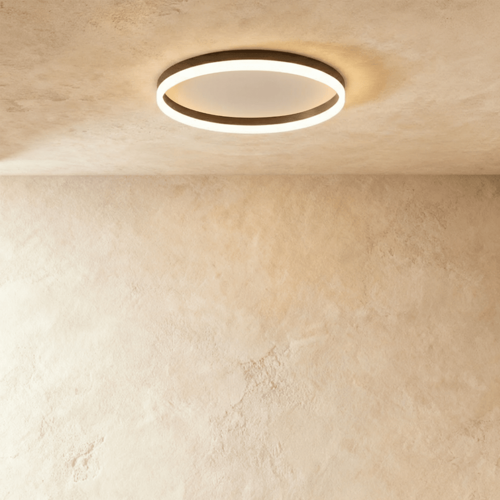 Clérachic slim black round ceiling light with a glowing acrylic ring and pale centre disc, flush on limewash plaster.
