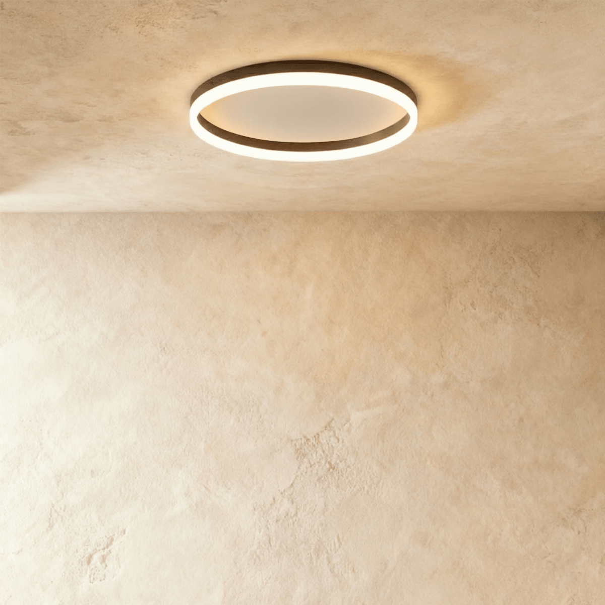 Clérachic slim black round ceiling light with a glowing acrylic ring and pale centre disc, flush on limewash plaster.
