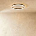 Clérachic slim black round ceiling light with a glowing acrylic ring and pale centre disc, flush on limewash plaster.